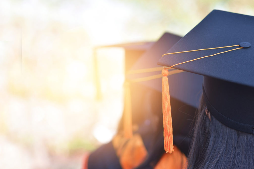 Trust God After Graduation. The back image of the graduates wearing a yellow tassel hat.