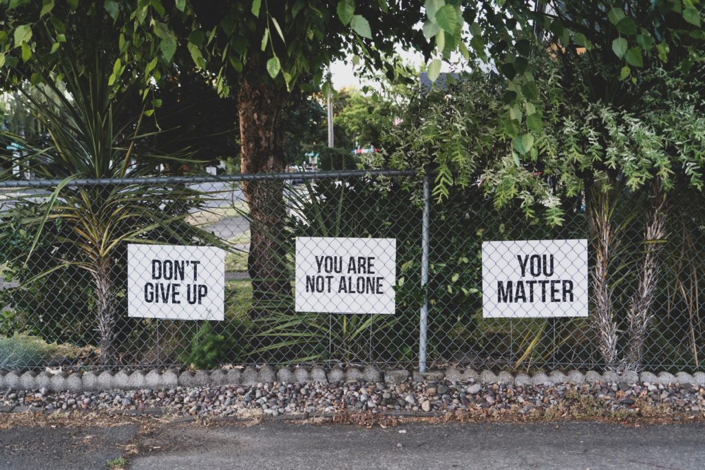 Three signs attached to a chain link fence that say, "Don't give up," "You are not alone," and "You matter". Scriptures to Encourage New Grads
