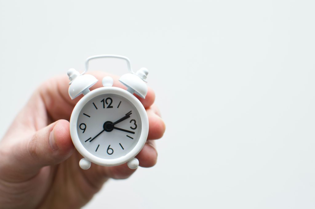 Hand holding small clock; time management tips