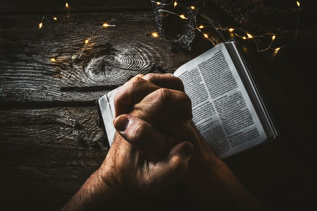 Prayer hands placed over an open Bible.